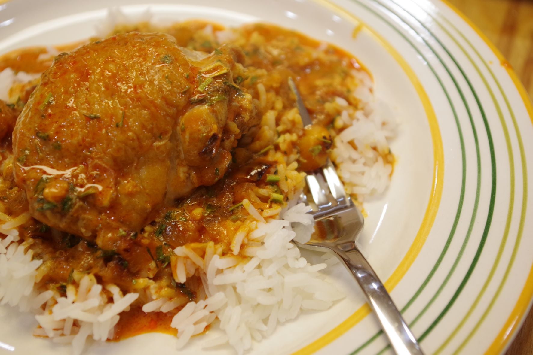 Butter chicken served over rice, on a plate with a fork